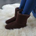 Chocolate sheepskin slipper boot, worn by model sat on an ivory sheepskin rug